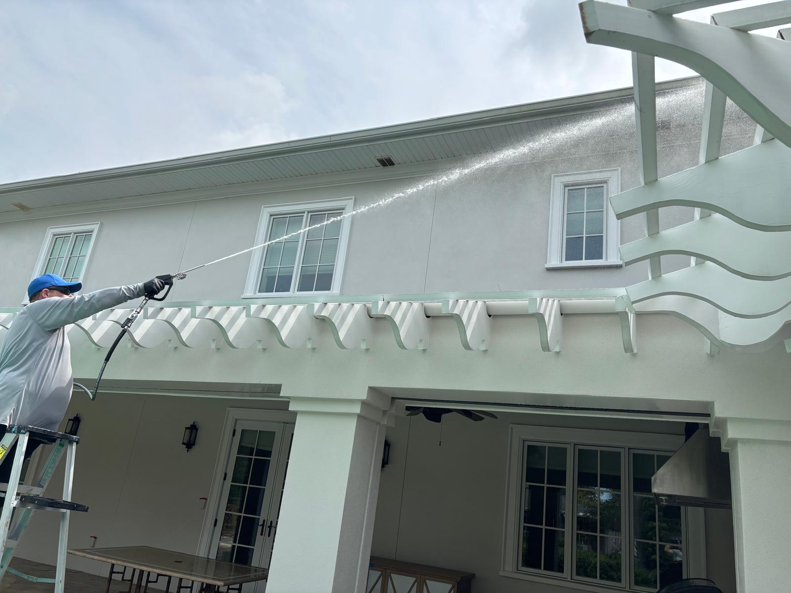 Technician rinsing a stucco exterior wall above a covered patio during a house washing project in Belleair, FL